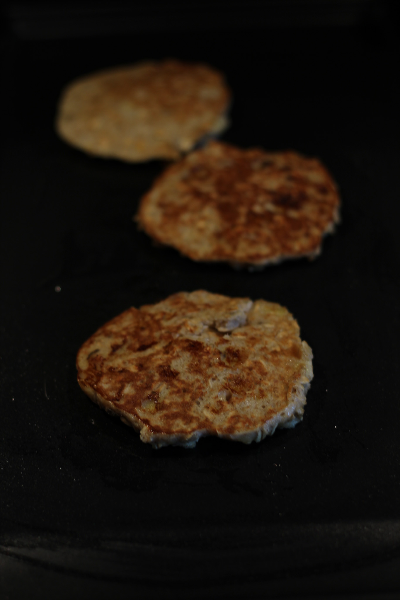 Banana oatmeal pancakes cooking on a griddle