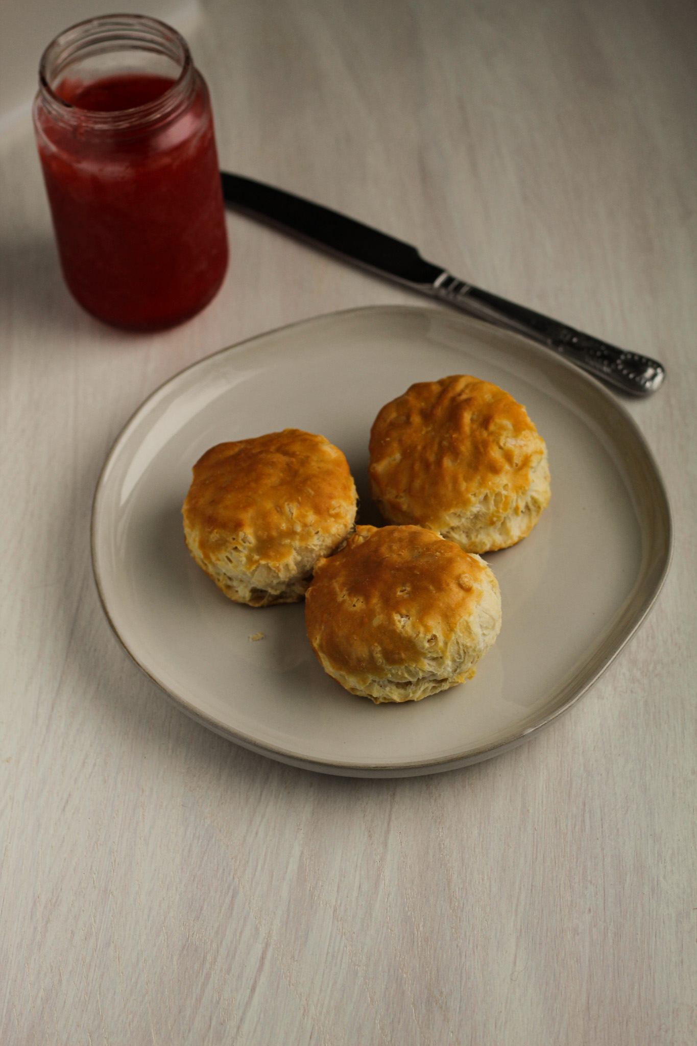 biscuits on plate next to jar of jam and butter knife